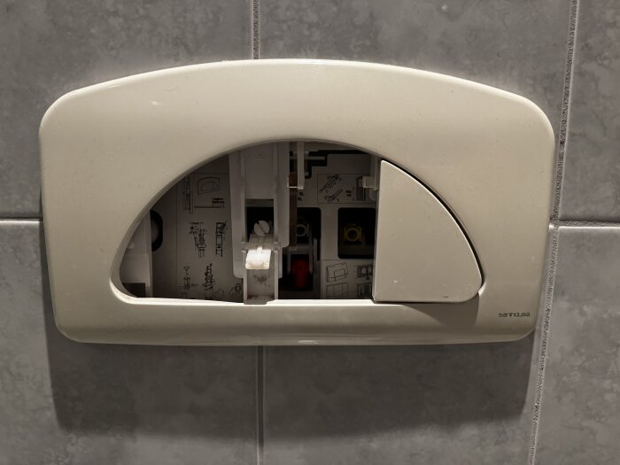 Väggmonterad Sanindusa spolpanel med trasig spolknapp, monterad på kakelvägg med synlig insida av cistern.
