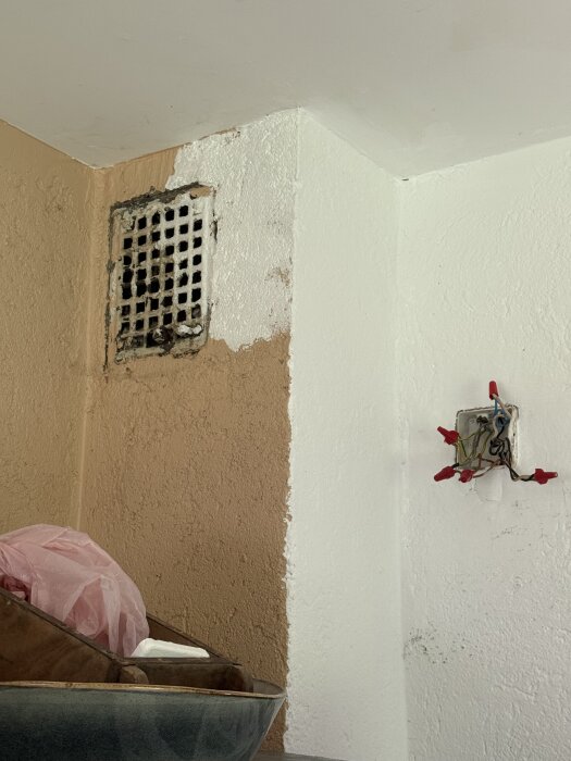 Vägg med vitmålat ventilgaller ovanför en köksbänk, omgiven av beige och vit vägg. Åsidosatt elbox med lösa kablar till höger.