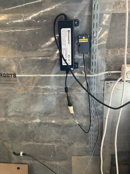 En installation av en Husqvarna Automower med ledningar och enheten märkt "Klippare" på en vägg med kabeldragning och kopplingsdosor.