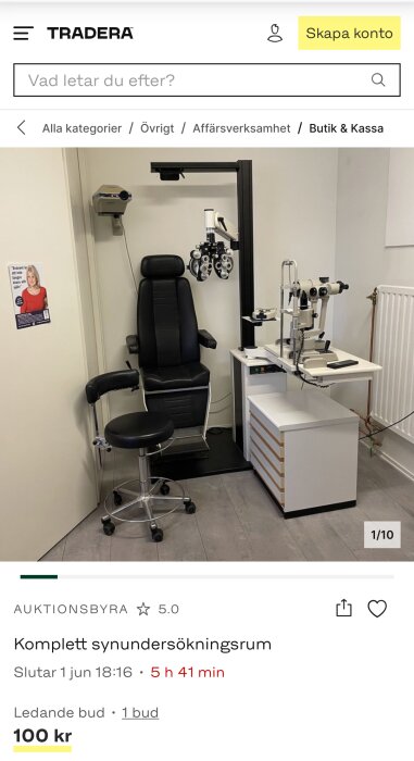 Komplett synundersökningsrum med undersökningsstol, optometrisk utrustning och instrument på en vit arbetsyta i en klinikmiljö.