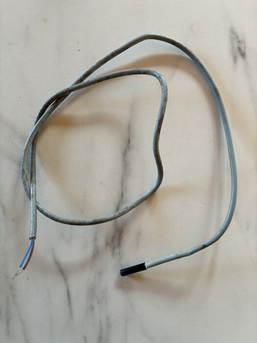 Sliten givare med avklippta kablar på ljus bakgrund, använd i en poolvärmepump.