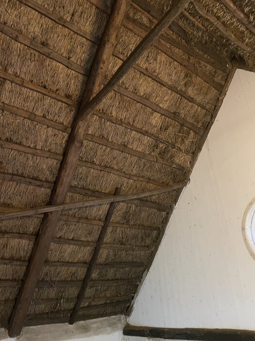 Innertaket i en gammal skånelänga med synliga träbjälkar och halm, som behöver renoveras för värme och stabilitet.