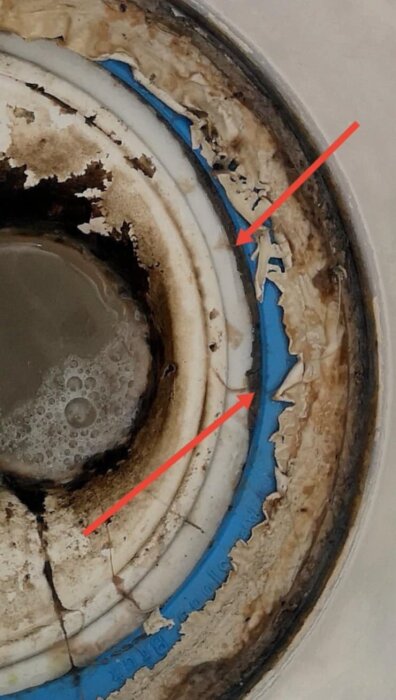 Avloppsbrunn med synligt tätskikt och klämring, pilar markerar områden med applicerat material, delvis skadade ytor runt brunnen.