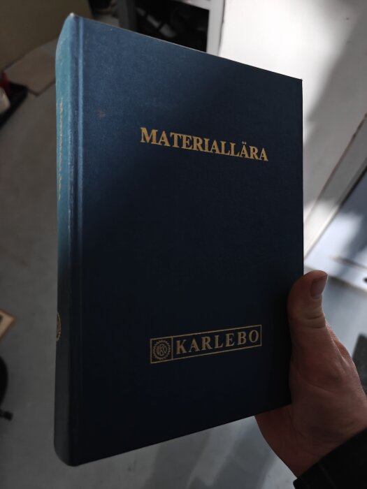 Boken "Materiallära" från Karlebo hålls i en hand.
