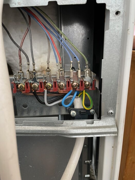 Anslutningar av fem färgade kablar inne i en spis, monterade med skruvterminaler.