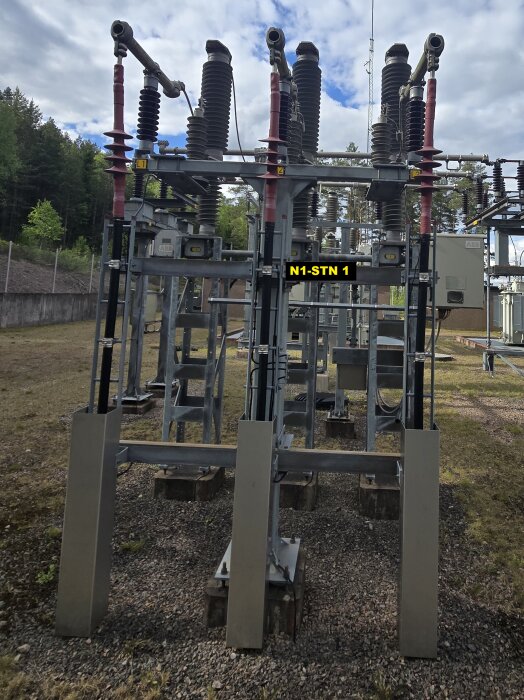 Utomhusbild av en kraftstation med högspänningsutrustning, inkluderande isolatorer och ledningar, märkta med "N1-STN 1" i förgrunden.
