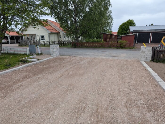 Uppfart med grusad yta och två murade stentornen på sidorna, med ett hus och träd i bakgrunden.