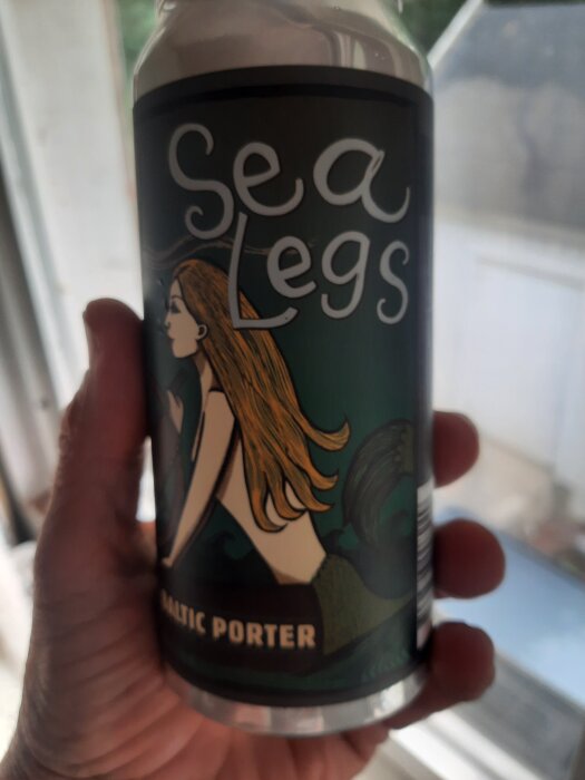En hand håller en burk med etiketten "Sea Legs Baltic Porter" och en bild av en sjöjungfru med långt hår.