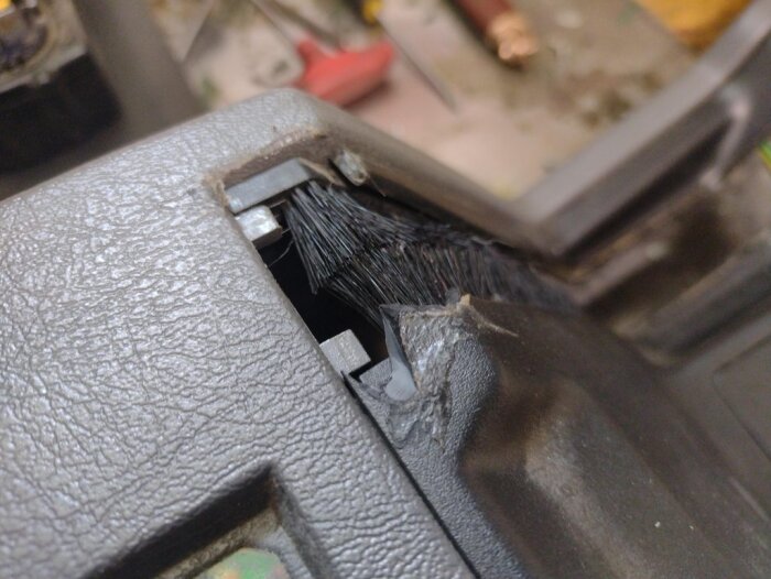 Sprucken centerkonsol från en Volvo 850 där plasten brutits upp, med försök till tidigare reparation synligt. Verktyg skymtas i bakgrunden.