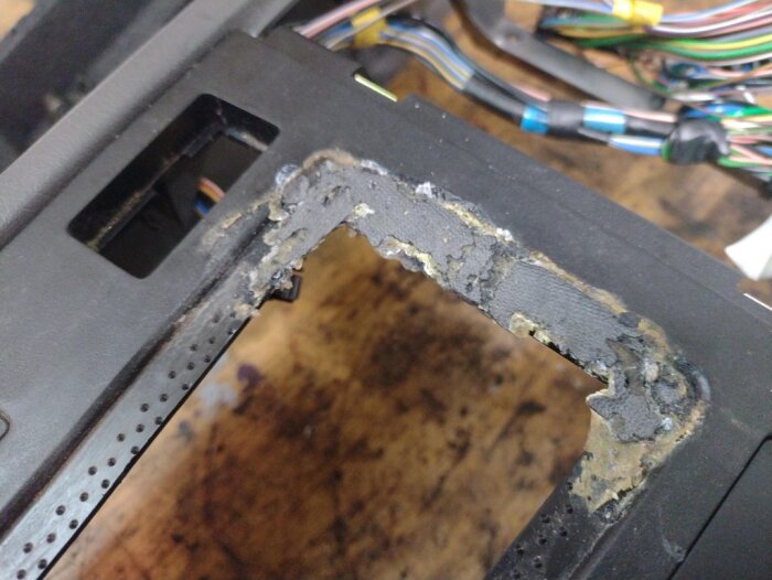 Centerkonsol i Volvo 850 med sprucken yta, delvis limmad och skadad, främst runt kanten där läderdamasken till växelspaken satt.