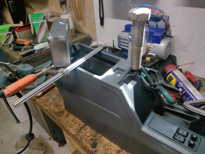 Centerkonsolen från en Volvo 850 är fastklämd i ett skruvstäd på en arbetsbänk för att reparera sprickor. Verktyg och material syns i bakgrunden.