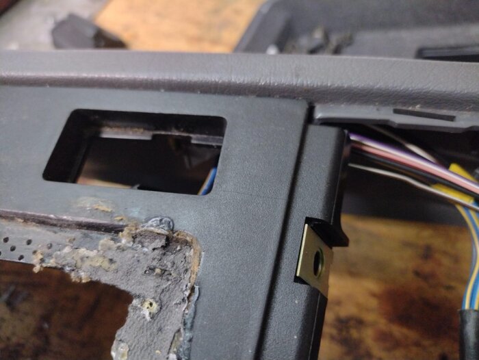 Centerkonsol från Volvo 850 med skadad yta och synliga sprickor. Gamla limrester och exponerade kablar syns. Reparation planeras.