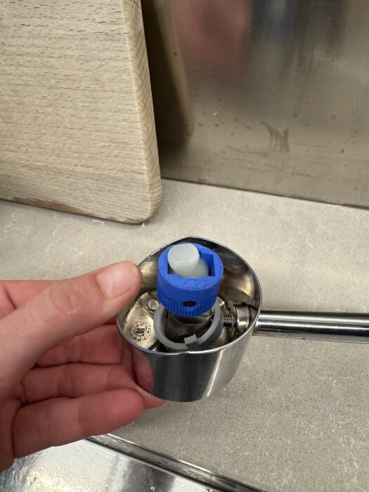 Närbild av en hand som håller ett borttaget handtag från en kökskran, med insidan av blandaren synlig.