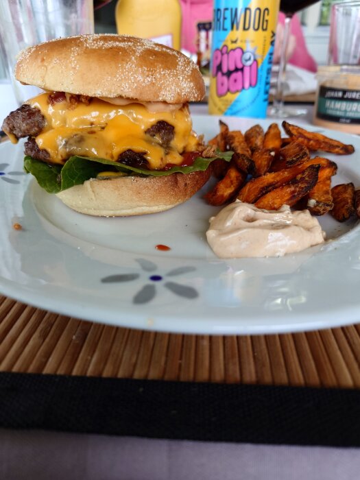 Hamburgare med smält ost, sallad och lök på en tallrik med sötpotatis pommes och dressing. I bakgrunden syns en Brewdog ölburk.