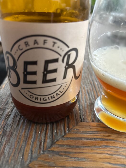 Flaska märkt "Craft Beer" och ett glas med skummande öl på ett träbord.