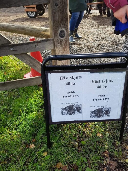 Skylt för hästskjuts för 40 kr vid grind med gräs runtom. Telefonnummer och Swish-nummer visas.
