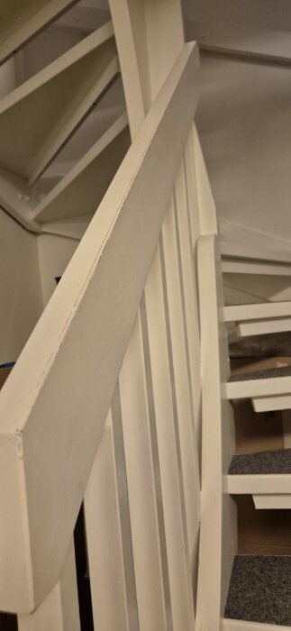 Vitt trappräcke som har börjat flagna på vissa ställen, sett från sidan med fokus på räckets ovansida och vertikala spjälor.