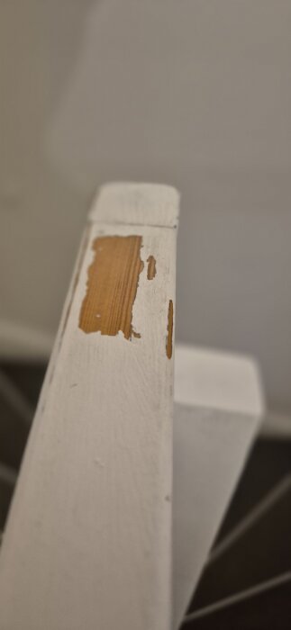 Slitet trappräcke med flagnande vit färg, avslöjande trä undertill, visa renoveringens utmaning.