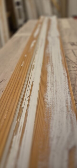 Slipad trappräcke med synlig vit färg och träyta, delvis avskavd efter bearbetning.