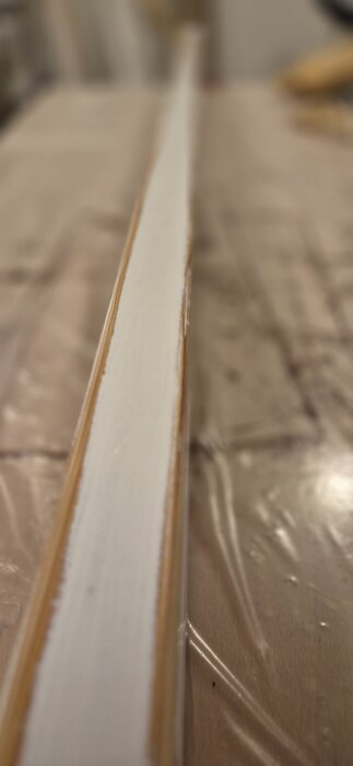 Slipad trappräcke med delvis bortskavd vit färg och synlig träyta, taget som del av ett DIY-målningsprojekt i ett hus.