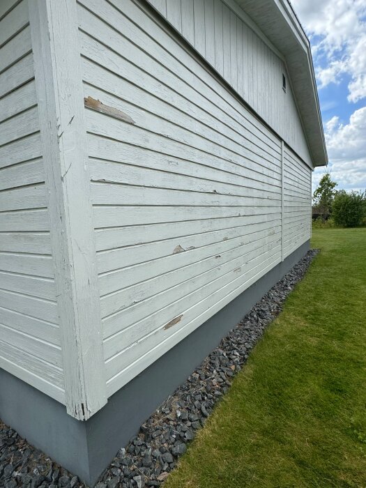 Vitmålad träfasad på hus från 1974 med färgavflagningar och skador. Rörelse- och slitageindikatorer syns på panelens yta.