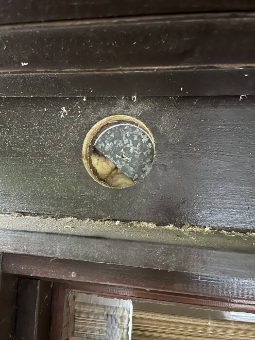 Rund öppning ovanför fönster med synlig plåt bakom asfaboard, förberett för friskluftsventil. Plåttjocklek ca 1 mm.