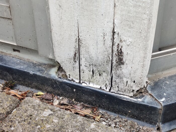 Murkna stolpar i uterum, synligt vid basen med färgsläpp och mögel, står direkt mot plattan med viss vatten- och fuktsamling.