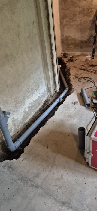 Nytt avloppsrör installerat i betonggolv med pågående renovering av köksstammar. Verktyg och byggmaterial syns runtom.