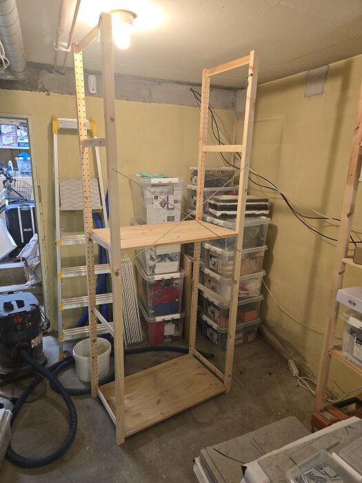 Trähylla byggs i ett hobbyrum med ljusgul vägg och förvaringslådor. En dammsugare står på golvet, samt en stege lutad mot väggen.