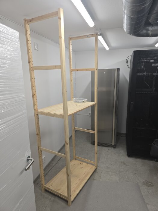 Trähylla pågår installation i ett maskinrum med klinkergolv, synliga ventilationsrör och belysning i taket. Hyllan är av märket Ivar.