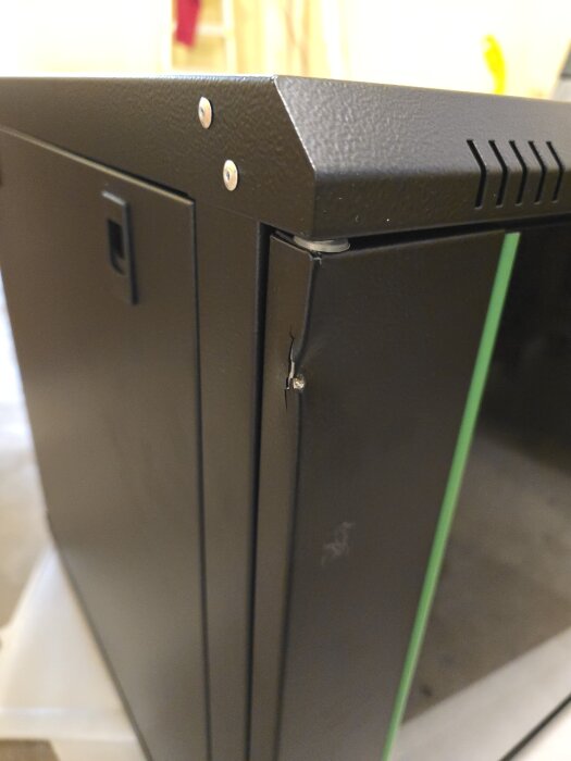 Skadat serverrack av märket Digitus med en intryckt dörrhörna, synligt sprickbildning vid fästpunkt.