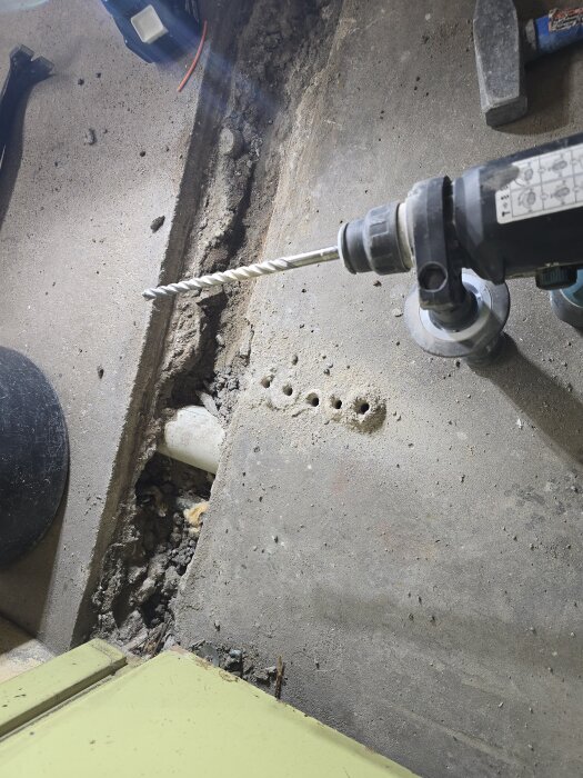 Borrmaskin och borrhål i betong för att blotta ett grunt avloppsrör under golvet i ett garage.