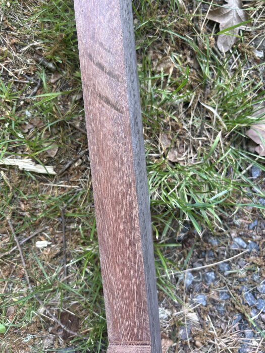 Närbild av en träbit med brun ådring på gräsig bakgrund, lagrad sen 80-talet.