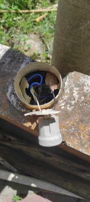 Elektrisk installation i ankelhöjd vid uteservering visar exponerade kablar i en metallask med en vit sockelhållare.