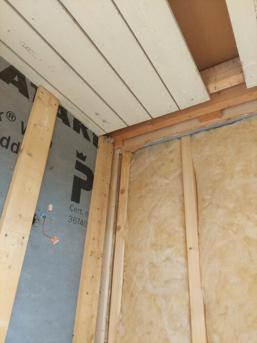 Vägg med träreglar och isolering, tak med träpaneler, synlig elinstallation. Inomhusrenovering; rivning och påregling syns.