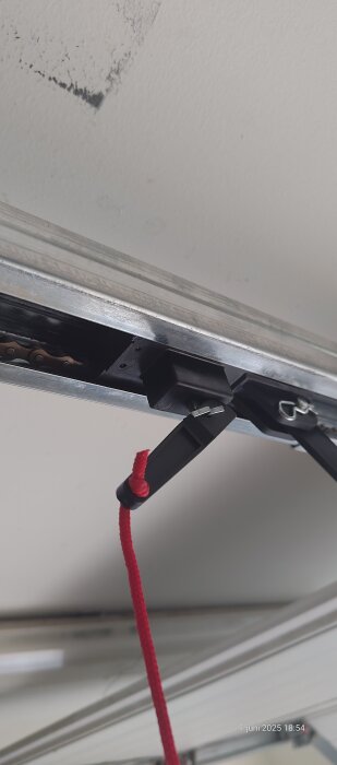 Närbild av en garageportkedja med en låsklump, röd snöre och drivmotorbeslag, sedd underifrån.