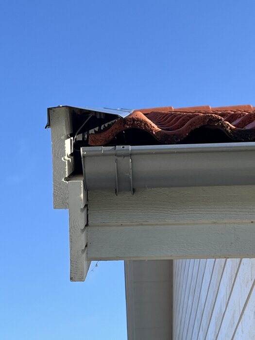 Närbild på ett hus hörn där vindskiveplåten inte når ner till takpannornas dal och takpannorna är felaktigt kapade.