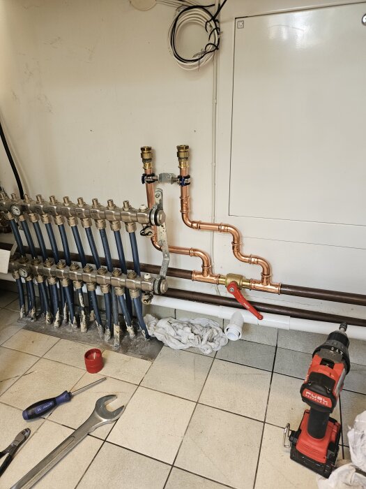 Vattenrör med nya presskopplingar installerade, omgivna av verktyg som skruvmejsel och borrmaskin på kaklat golv i en verkstadsmiljö.