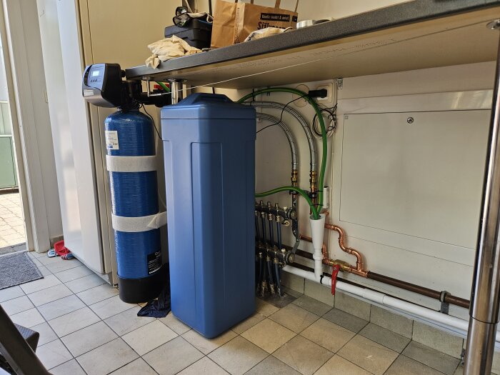 Vattenfilterinstallation under diskbänk med nya presskopplingar och ett blått filterhölje. Koppartuber och gröna slangar synliga.