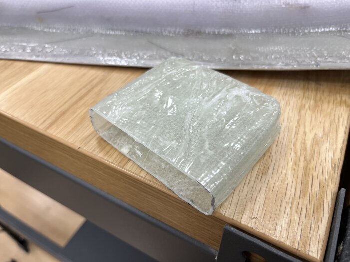En plastad ficka för låskista i glasfiber och epoxi ligger på en arbetsbänk av trä.