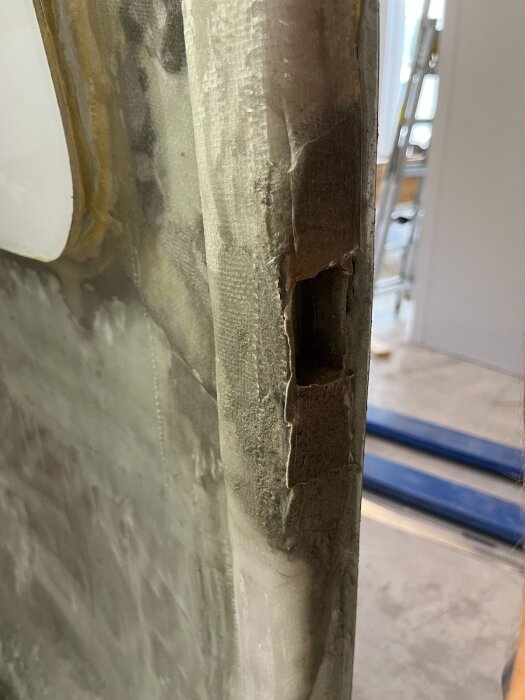 Utfräst hål i förstärkt dörrbalk, förberett för montering av låskista, med synliga lager av glasfiber och epoxy.
