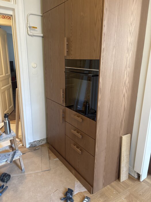 Köksinstallation med högskåp för kyl, frys och ugn, verktyg synliga på golvet, renoveringsarbete pågår.