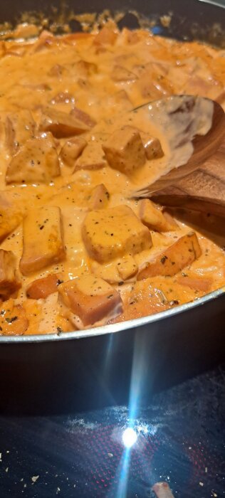 Krämig kyckling Stroganoff i en panna med träsked, med bitar av kyckling och örtkryddor synliga i såsen.