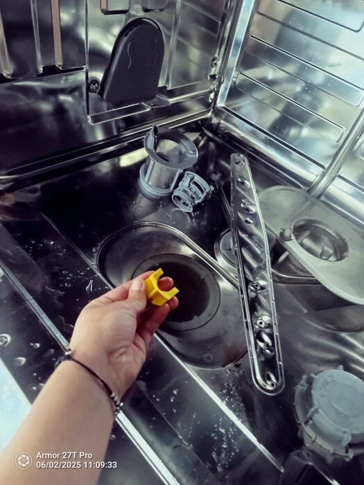 Hand håller gul del framför diskmaskinens pumpimpeller.