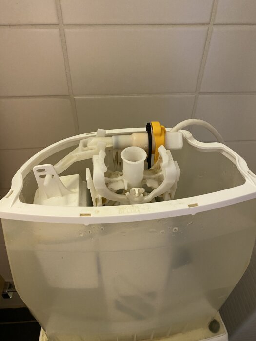 Flottörkontroll med svart buntband i öppen toalettcistern, vit och gul komponent syns.