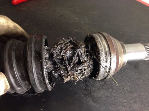 En ATV-axel med slitna och smutsiga damasker, trasig gummibälg med skräp intrasslat i mekanismen på ett verkstadsbord.