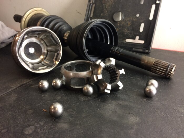Delar av en CV-led, inklusive kulor och andra komponenter, ligger utspridda på ett bord i ett garage.