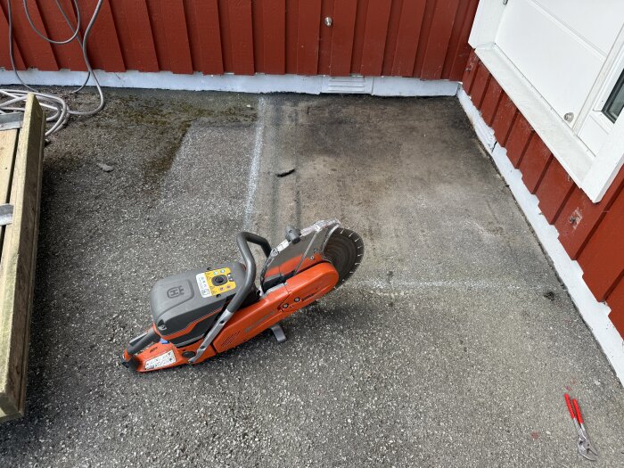 Bild av en asfalttrappa under bearbetning. En kapmaskin och en tång ligger på marken framför en röd träfasad.