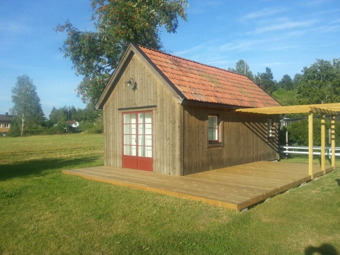 Garage ombyggt med järnvitriol och tegelpannor, stående på en trätrall. Bakgrund av grön gräsmatta och ett träd.