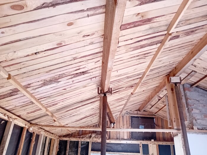 Invändigt tak under renovering med synliga sparrar och råspont i en liten stuga, med uppstöttade förstärkningar och reglar.